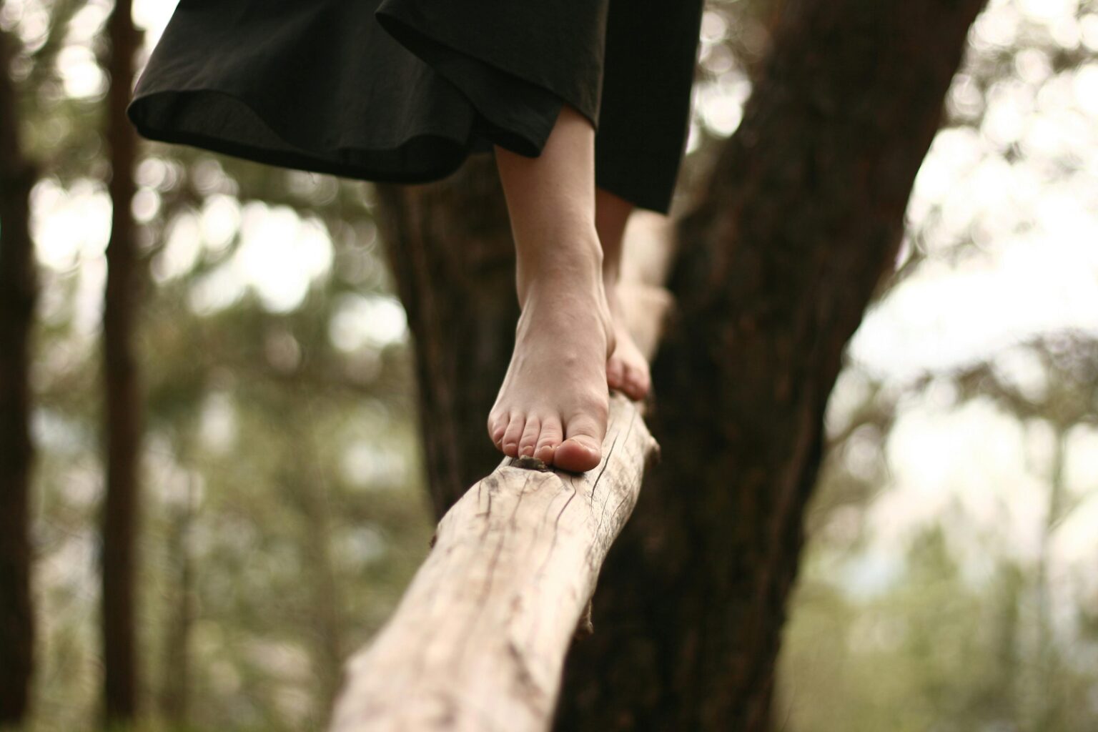 A woman walks barefoot on a log in a serene forest setting, capturing balance and focus.