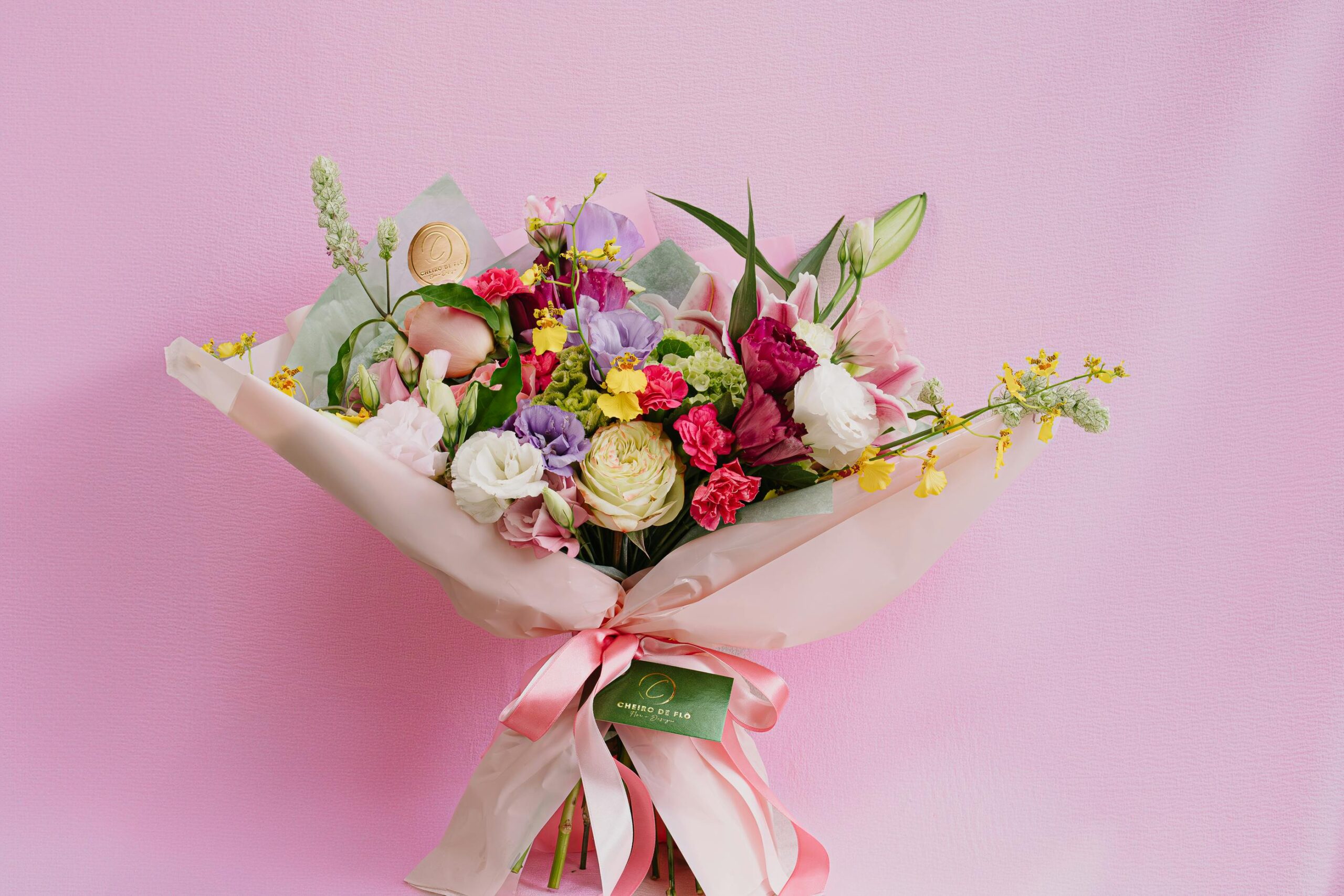 Charming mixed flower bouquet featuring roses and carnations against a pink backdrop.