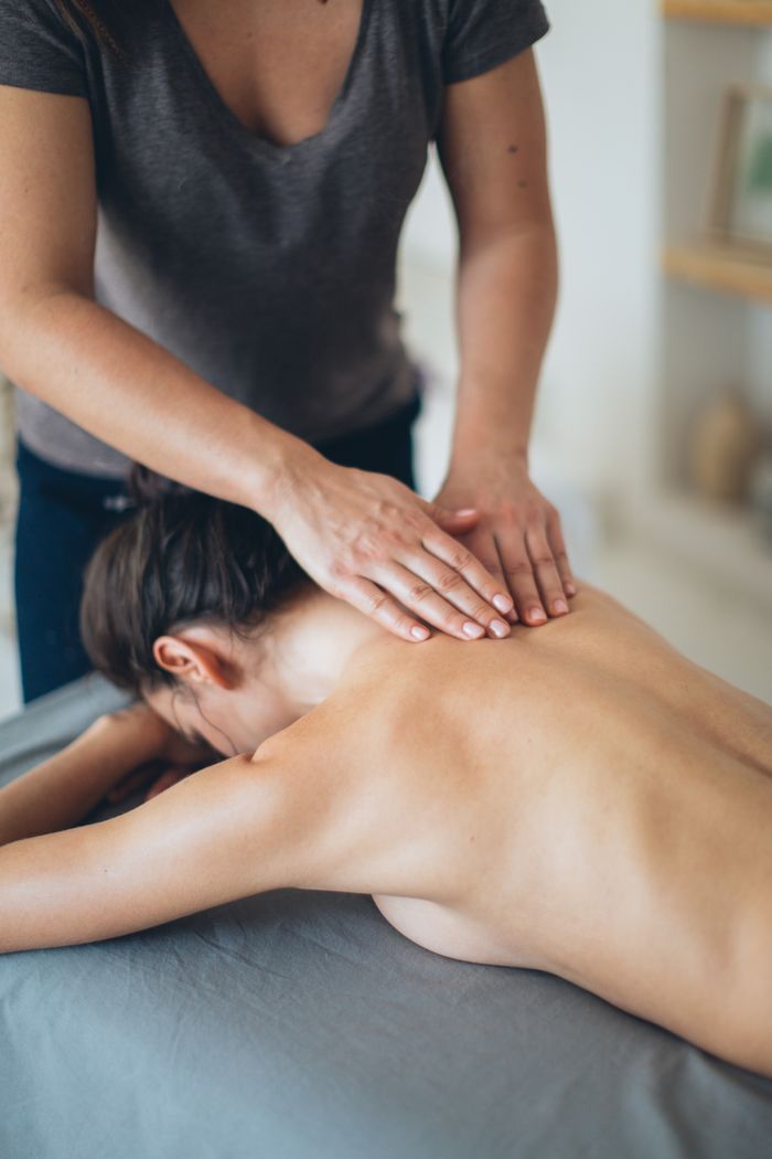 From above of anonymous massage therapist in gray t shirt rubbing back of unrecognizable woman during spa session in cozy room